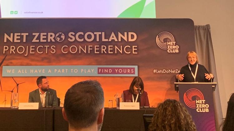 Speakers of the Net Zero Scotland Conference, two people sat on panel with a speaker on the podium.